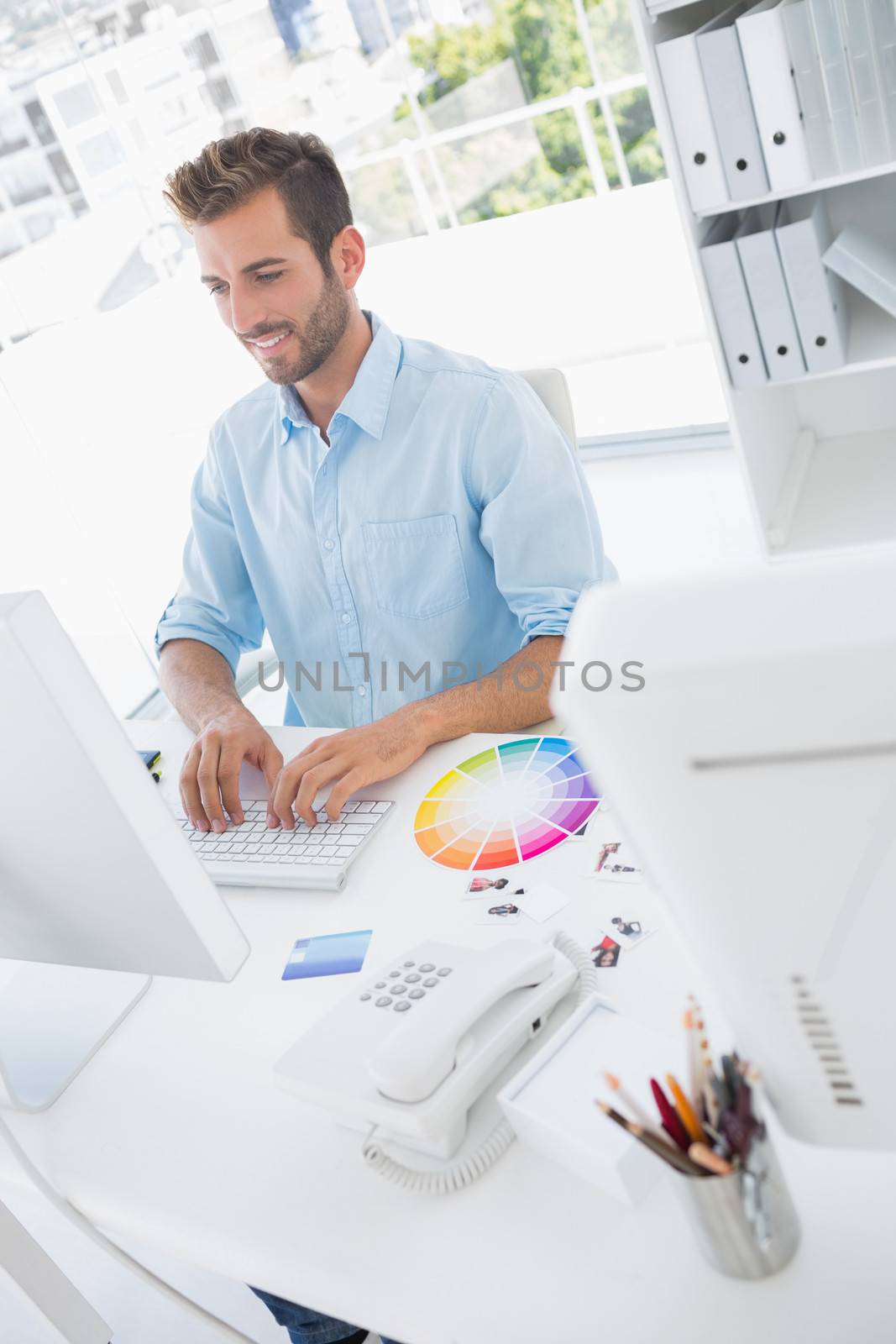 Smiling casual male photo editor using computer in the office
