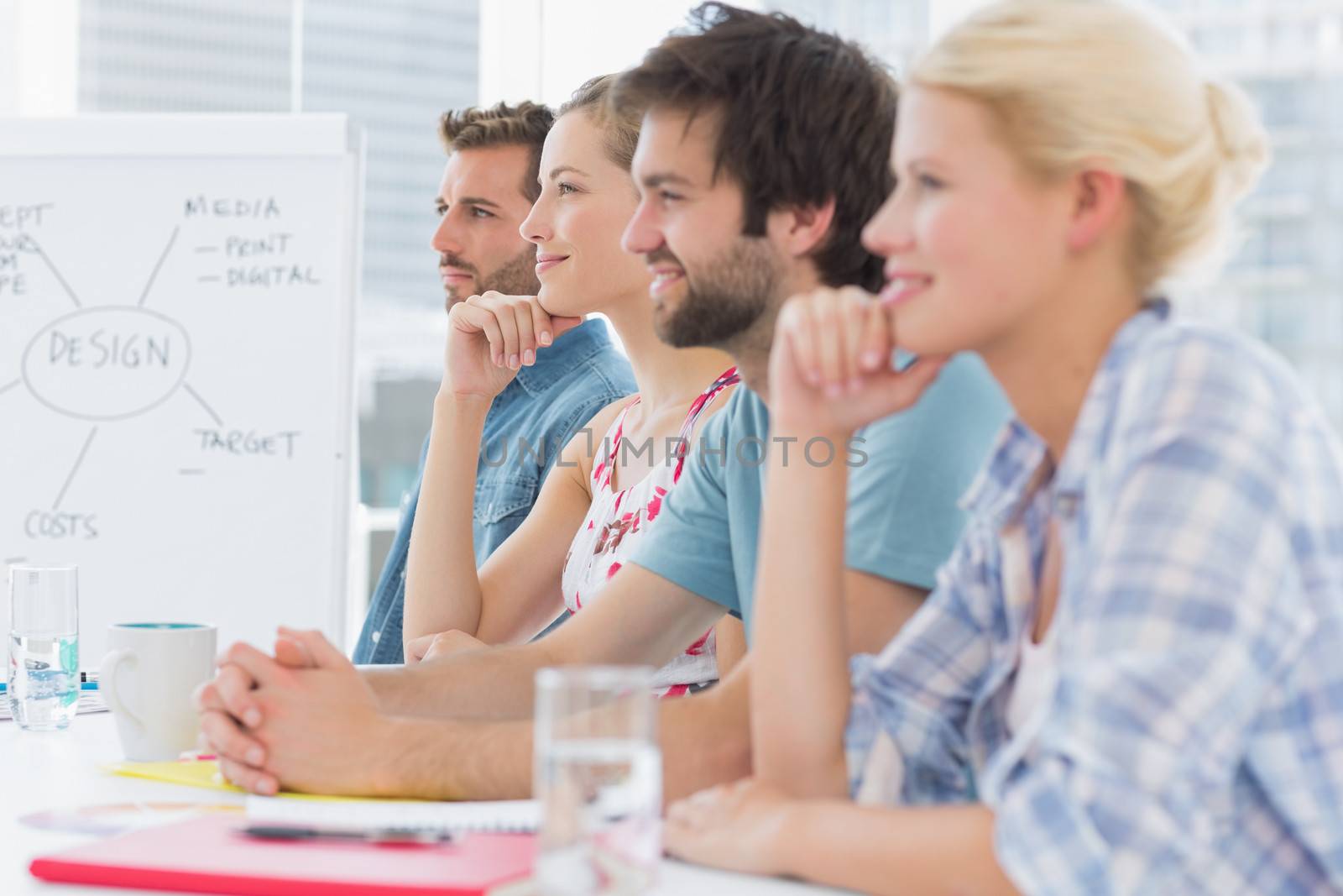 Group of smiling artists sitting in row during meeting at office