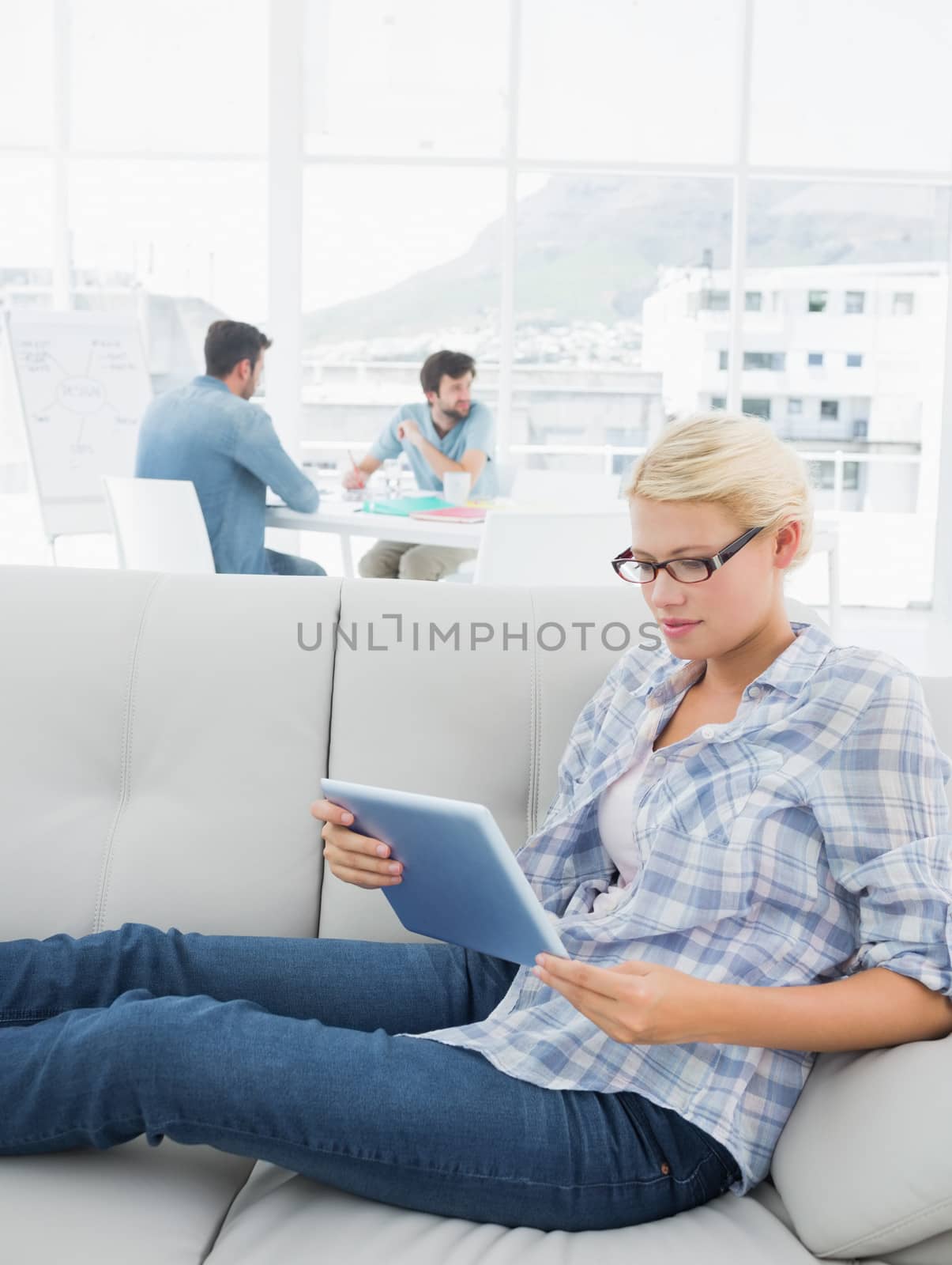 Woman using digital tablet with colleagues in background at creative office by Wavebreakmedia