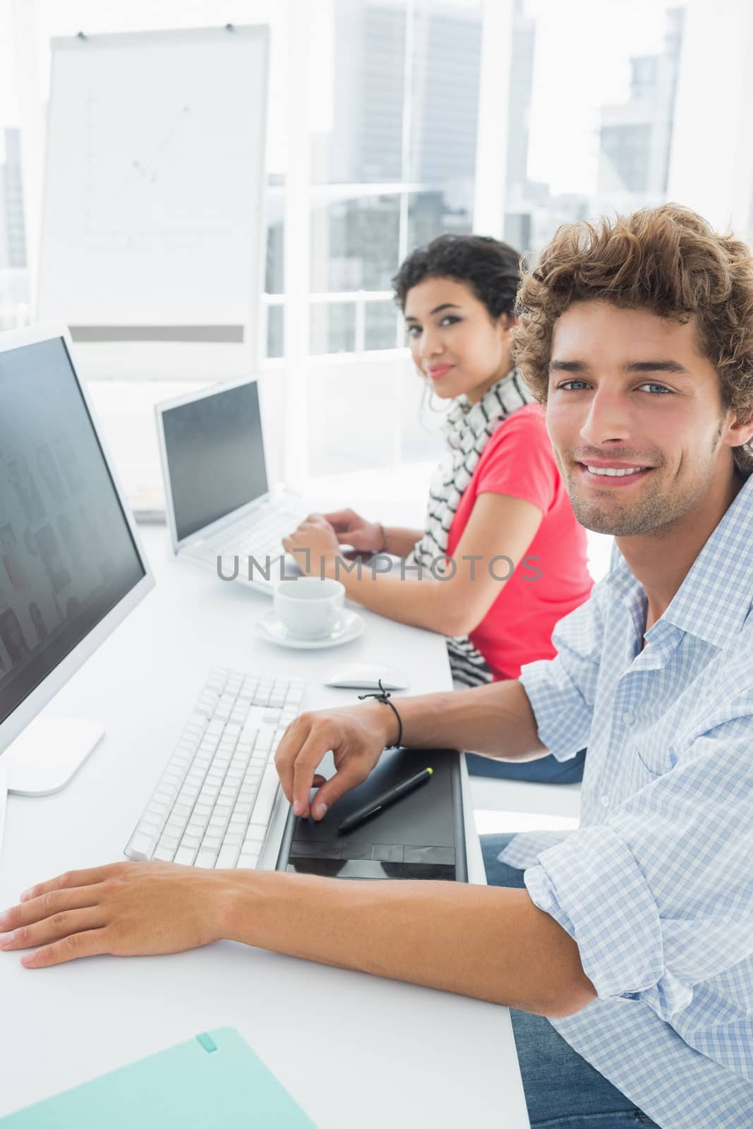 Side view portrait of a casual couple using computers in a bright office