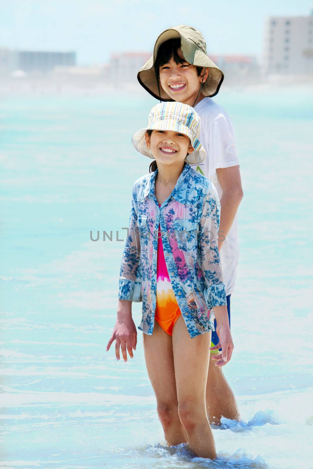 Two children wearing hats, playing in water's edge of ocean