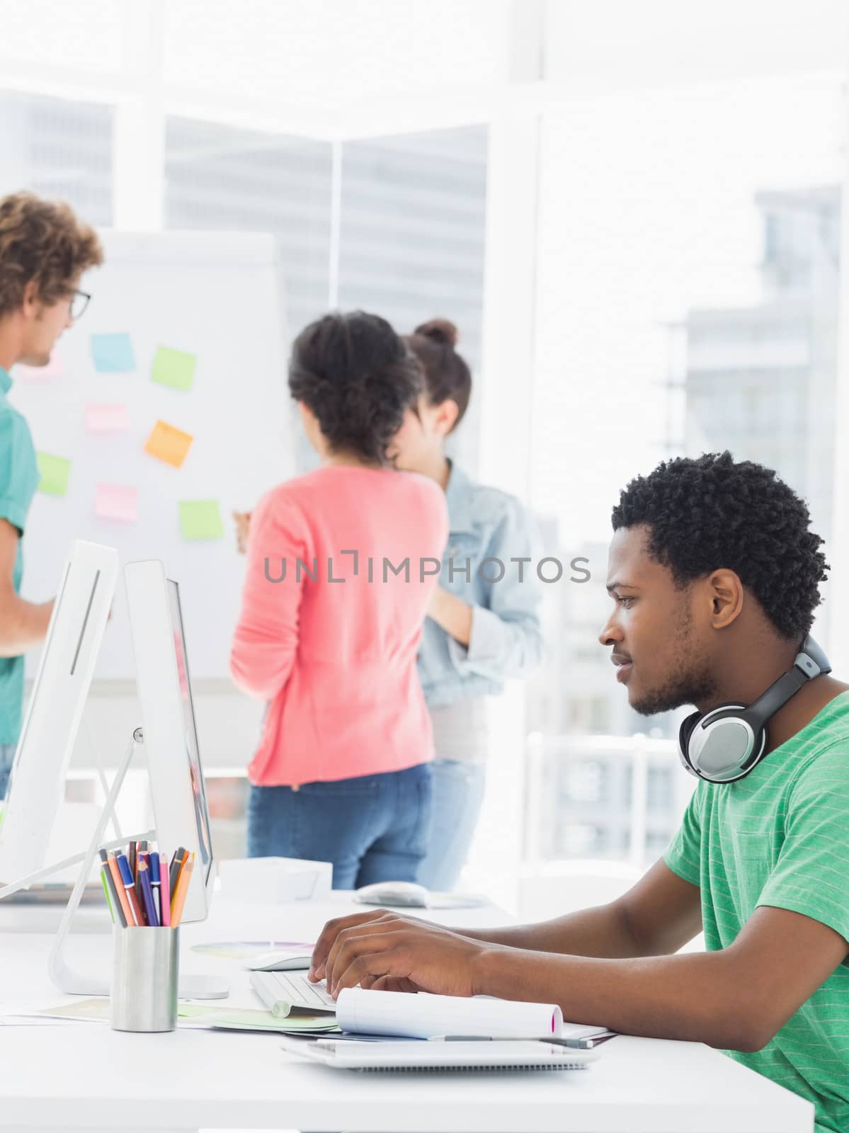 Casual man using computer with colleagues behind in office by Wavebreakmedia