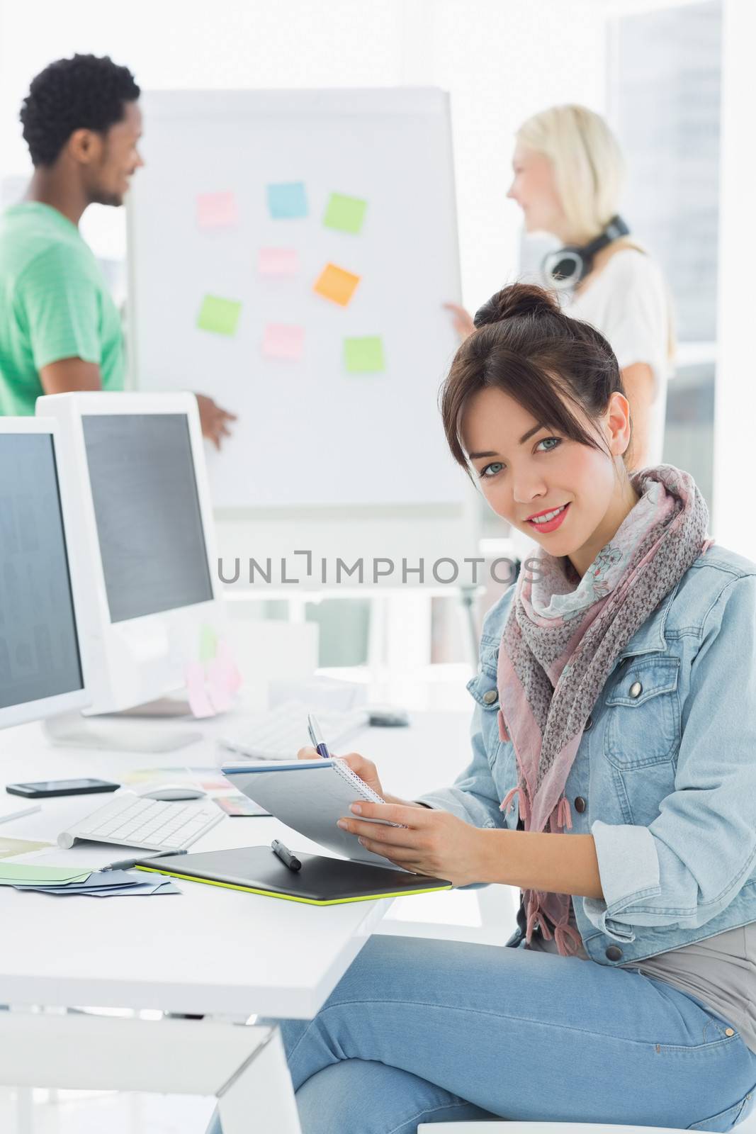 Portrait of an artist drawing something on graphic tablet with colleagues behind at the office