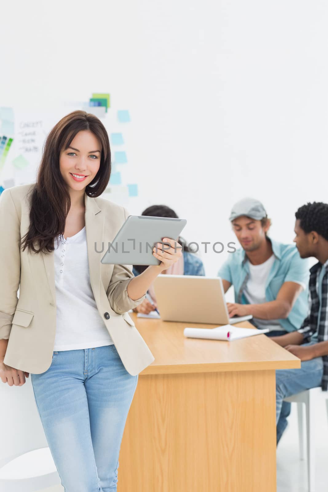 Casual woman using digital tablet with group of colleagues behind in a bright office