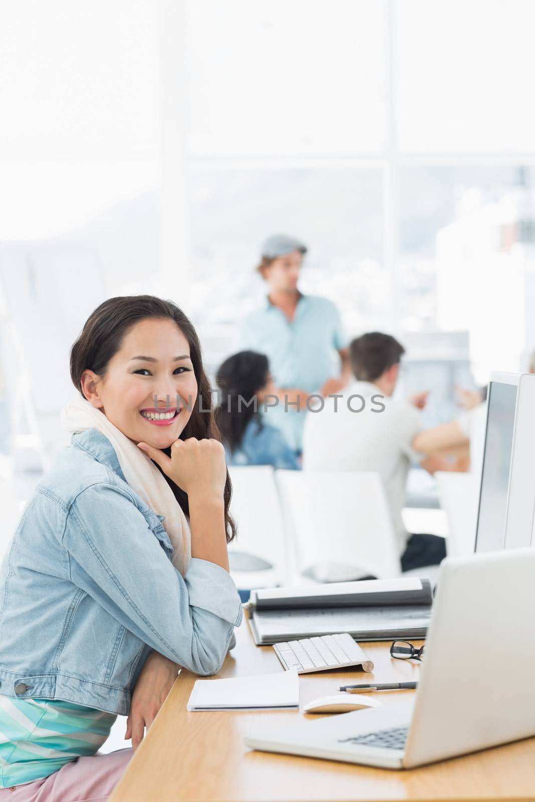 Portrait of a casual young woman with group of colleagues behind in a bright office