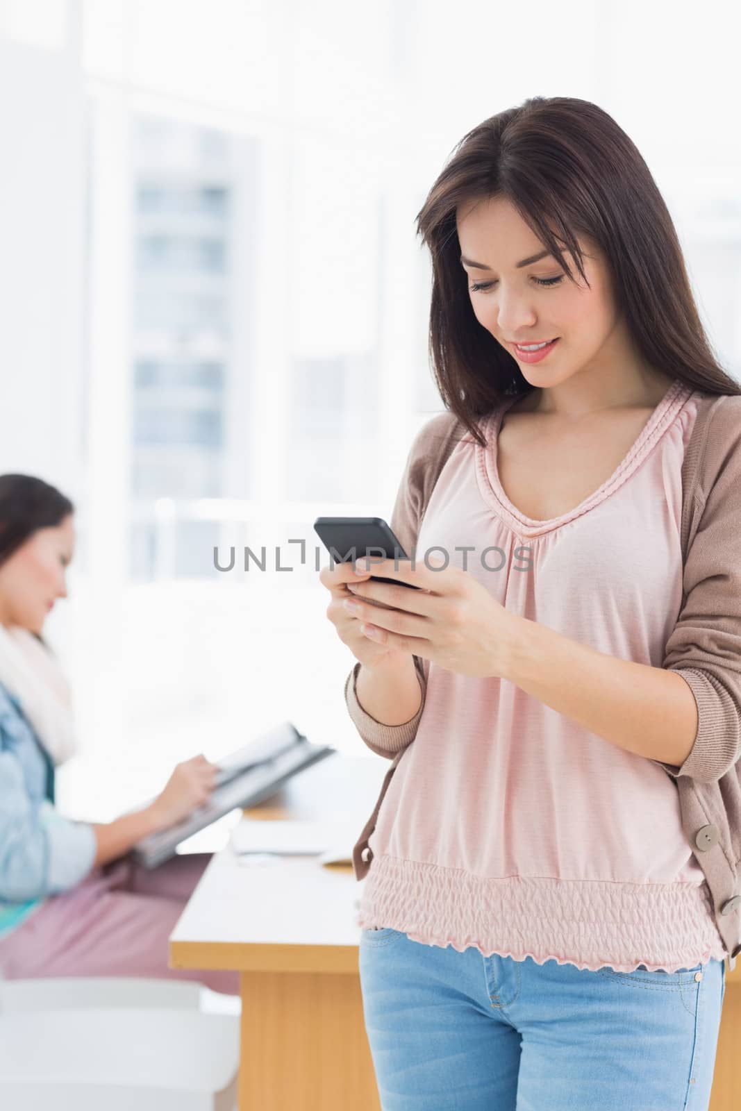 Casual young woman text messaging in a bright office