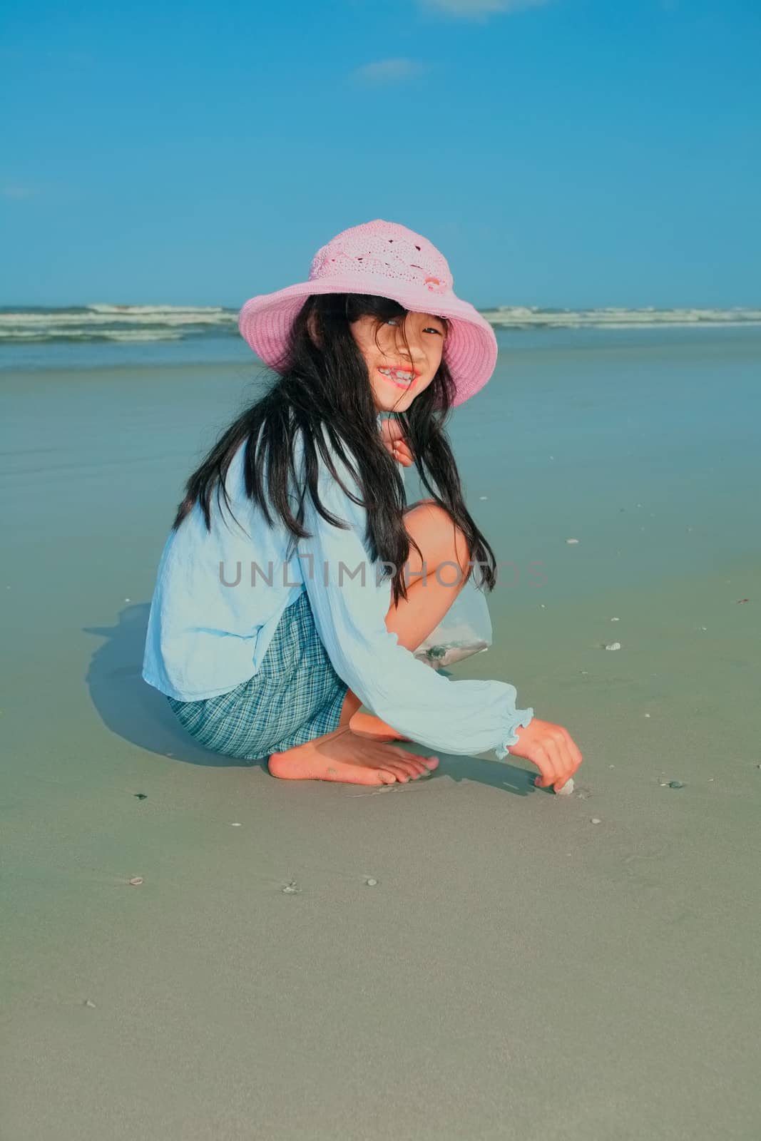 Little Asian girl looking for seashells on beach