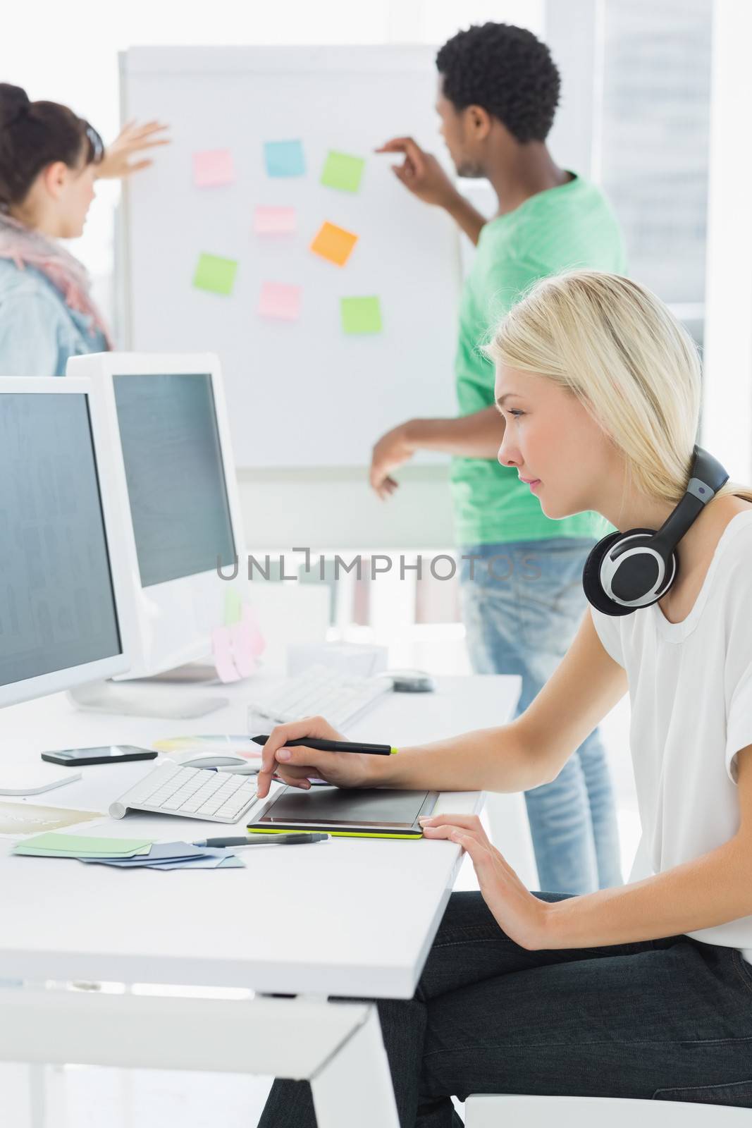 Side view of an artist drawing something on graphic tablet with colleagues behind at the office