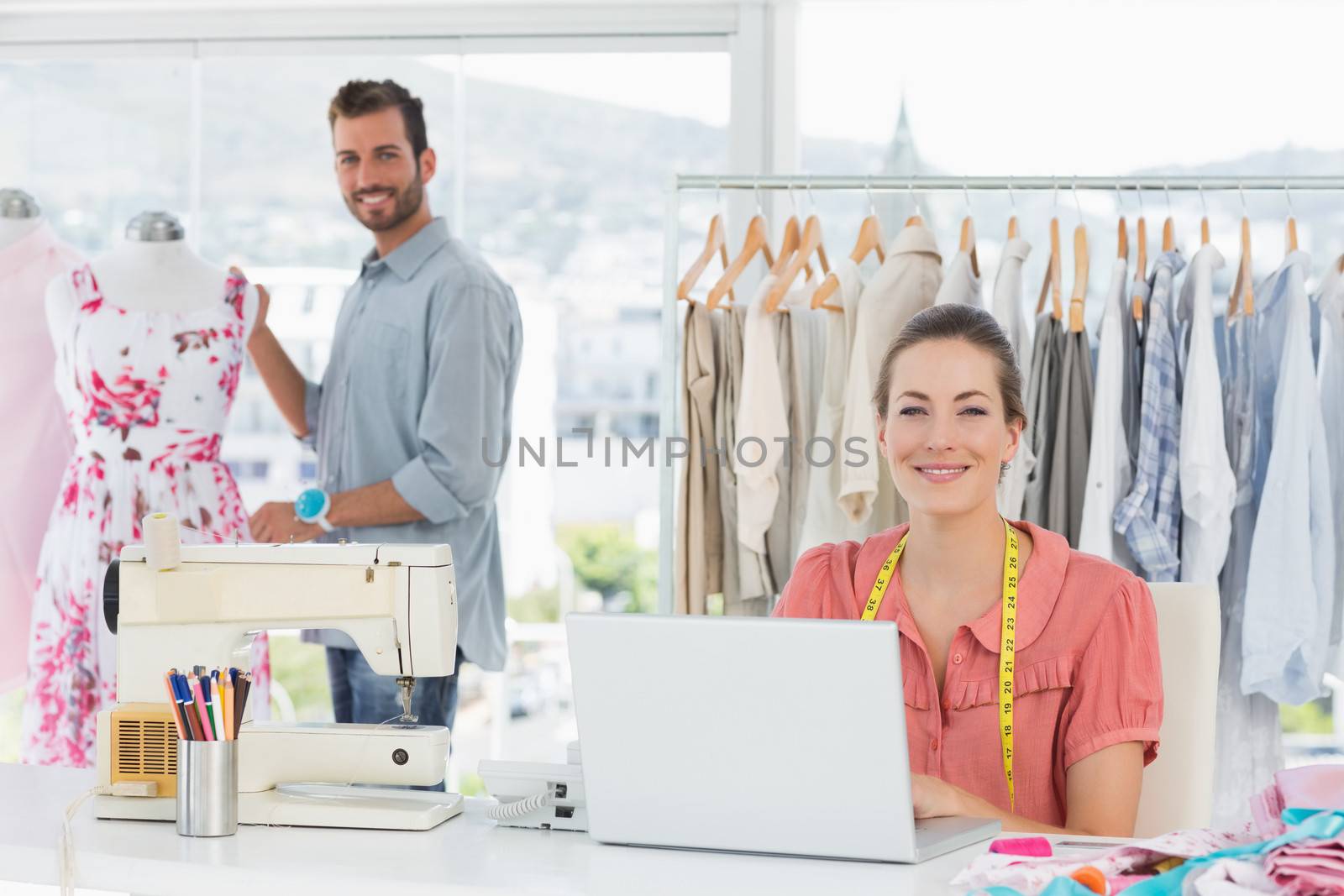 Young woman using laptop with male fashion designer working in background at the studio