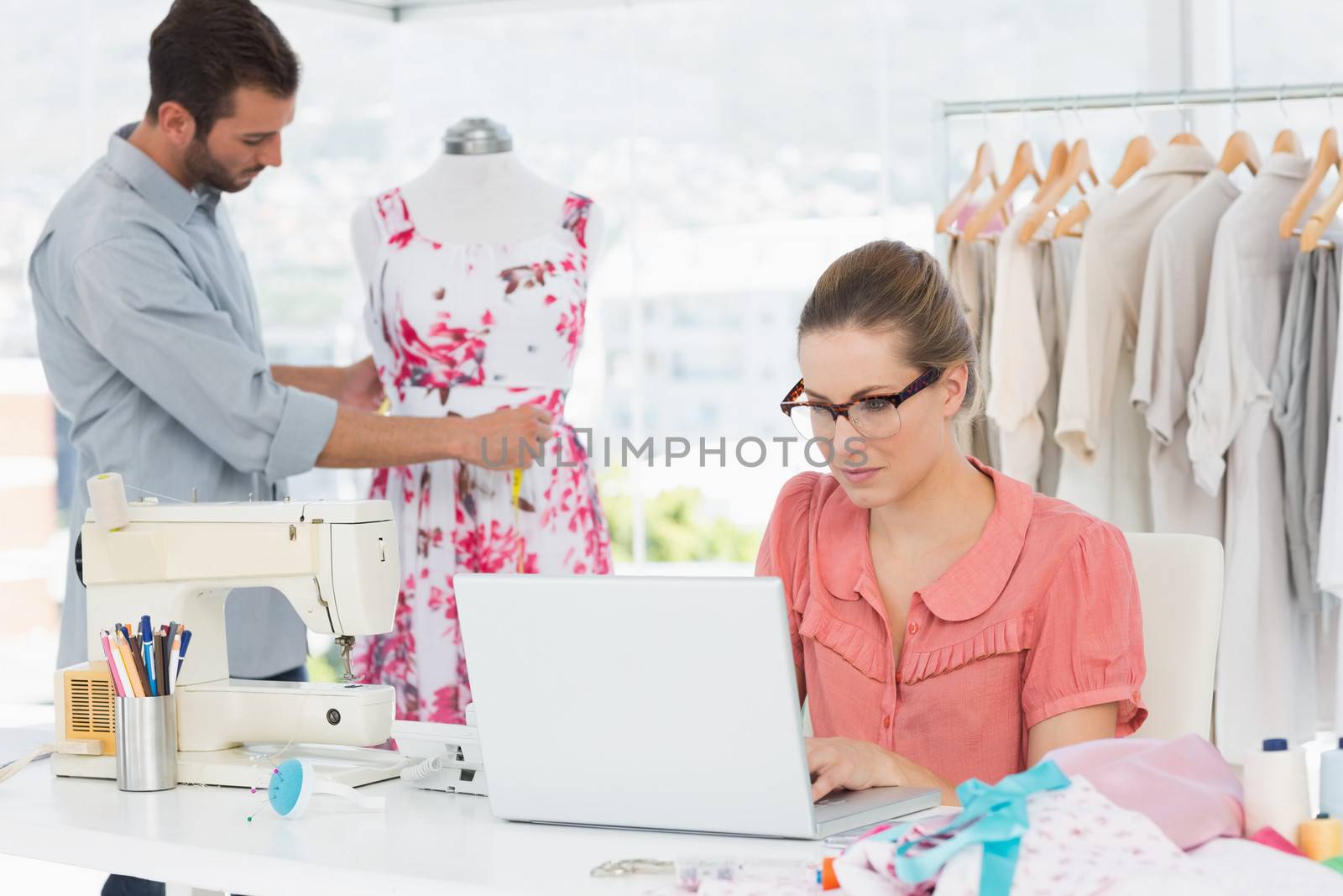 Young woman using laptop with male fashion designer working in background at the studio