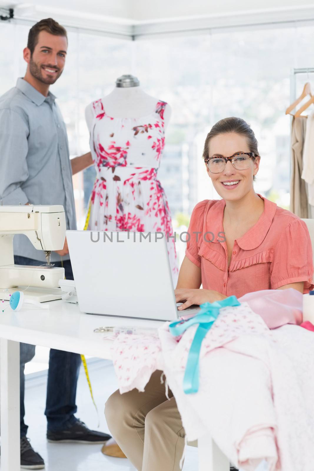 Young woman using laptop with male fashion designer working in background at the studio