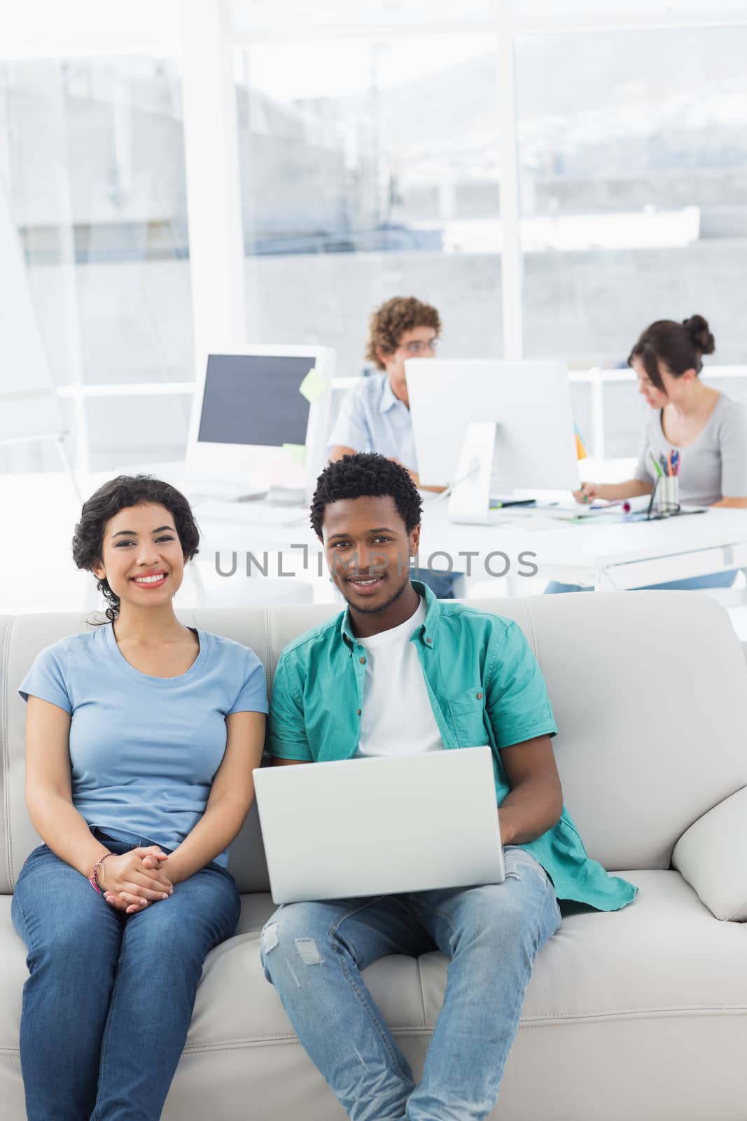 Couple using laptop with colleagues at creative office by Wavebreakmedia