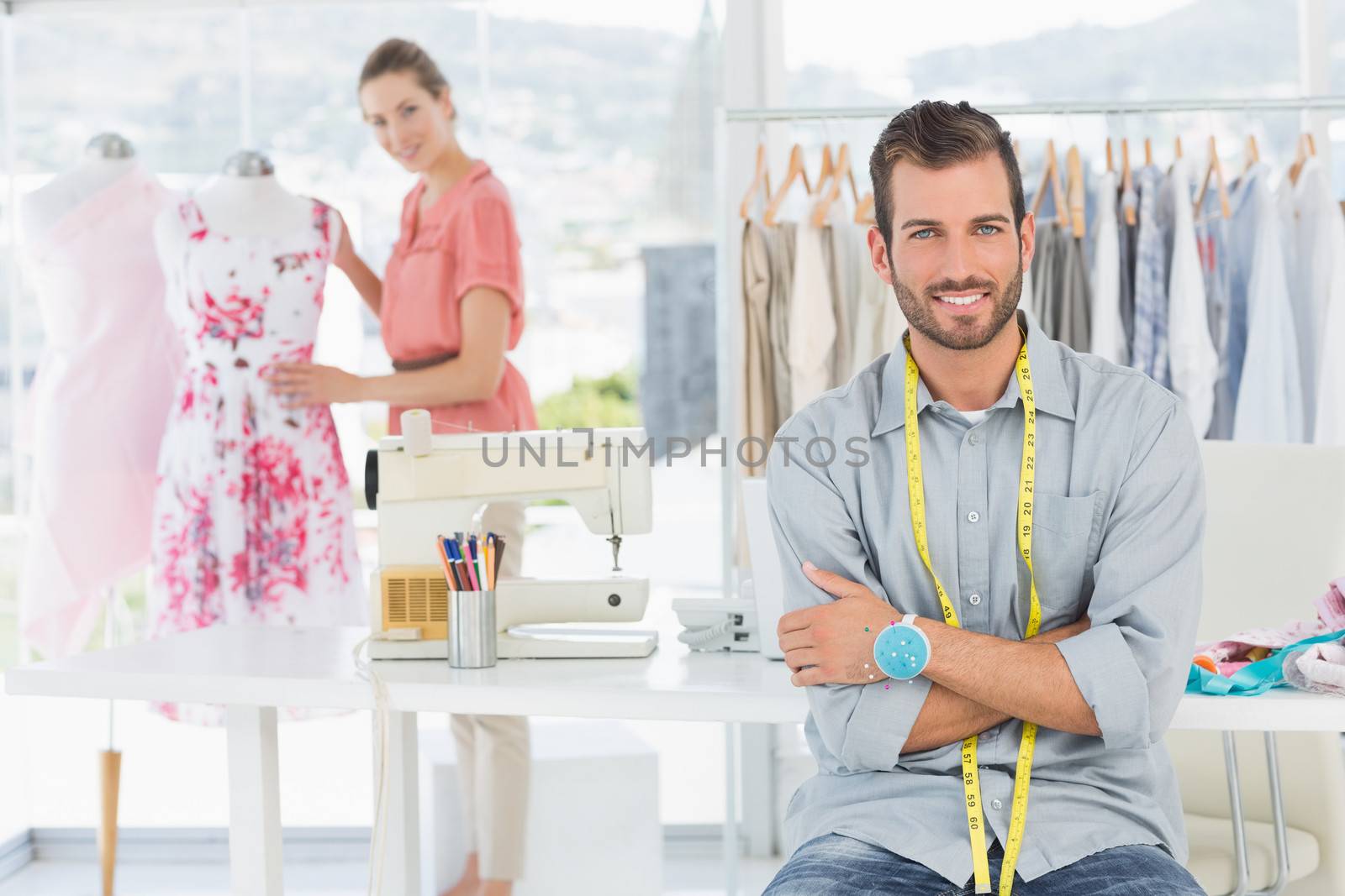 Portrait of a young man with female fashion designer working in background at the studio