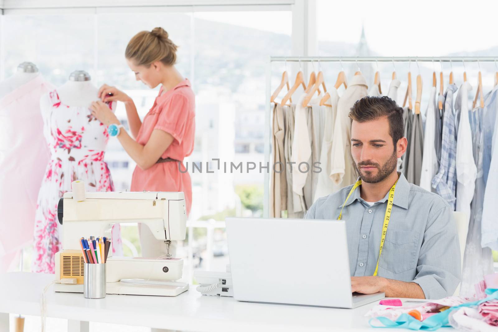 Young man using laptop with female fashion designer working in background at the studio