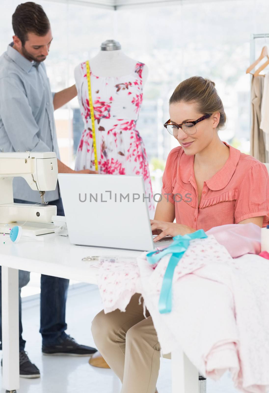 Young woman using laptop with male fashion designer working in background at the studio