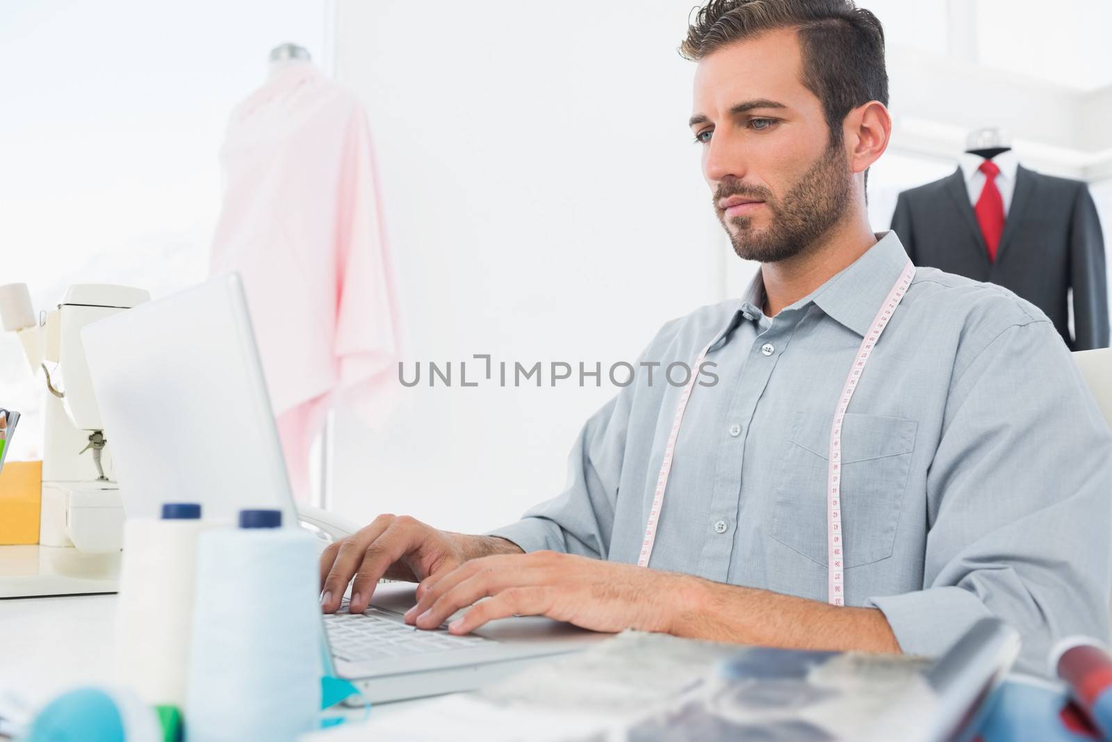 Young male fashion designer using laptop in the studio