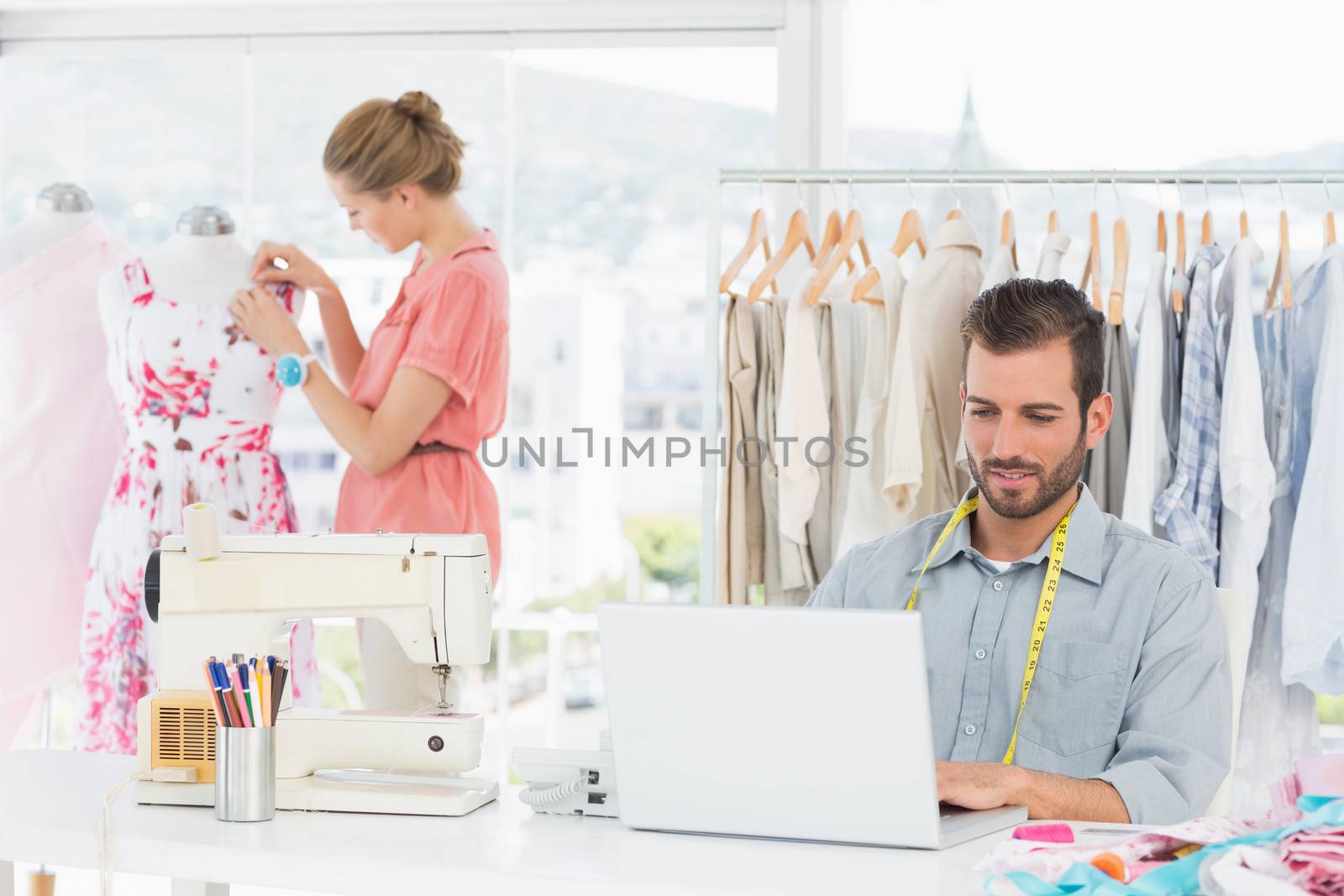 Young man using laptop with female fashion designer working in background at the studio