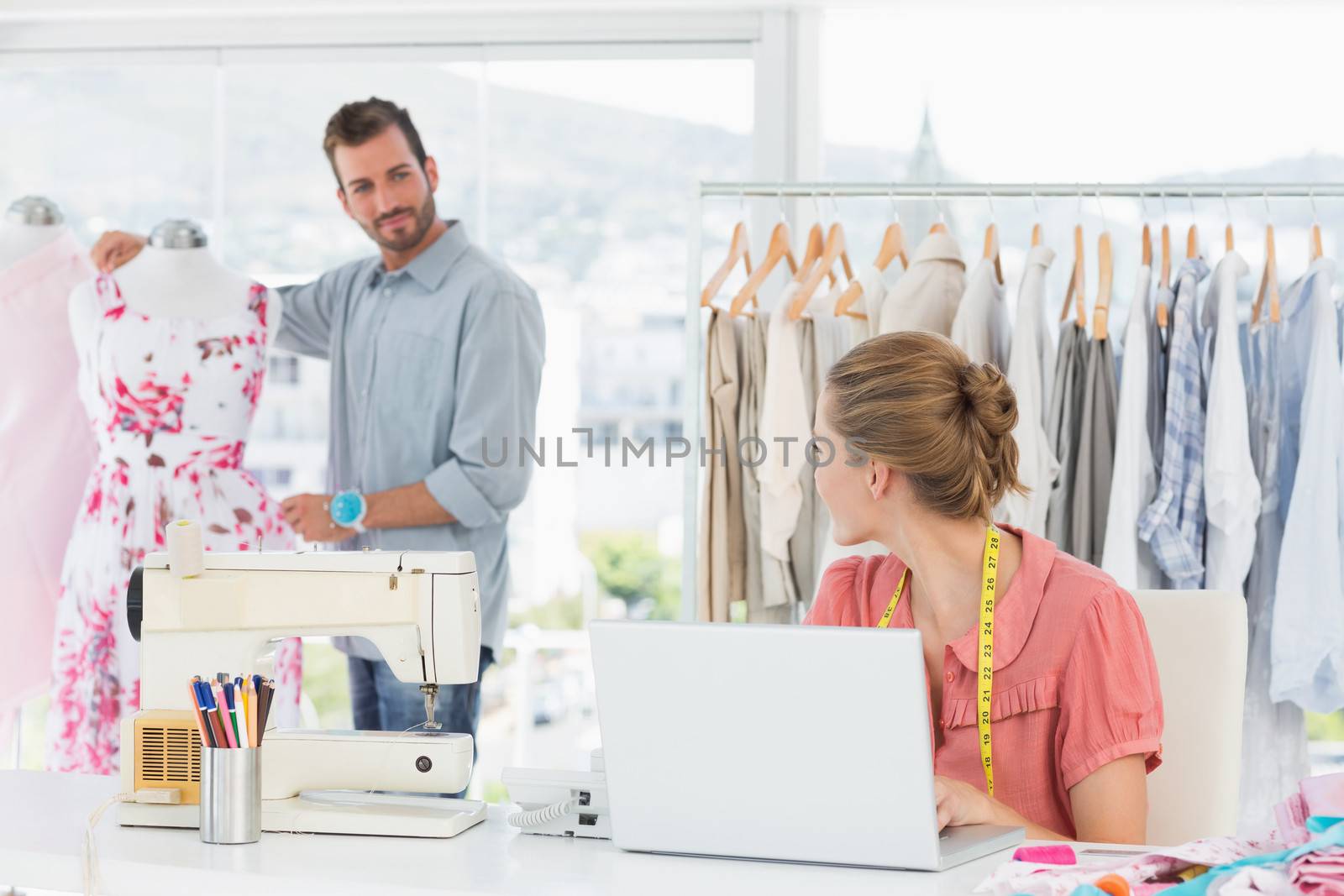 Young woman using laptop with male fashion designer working in background at the studio