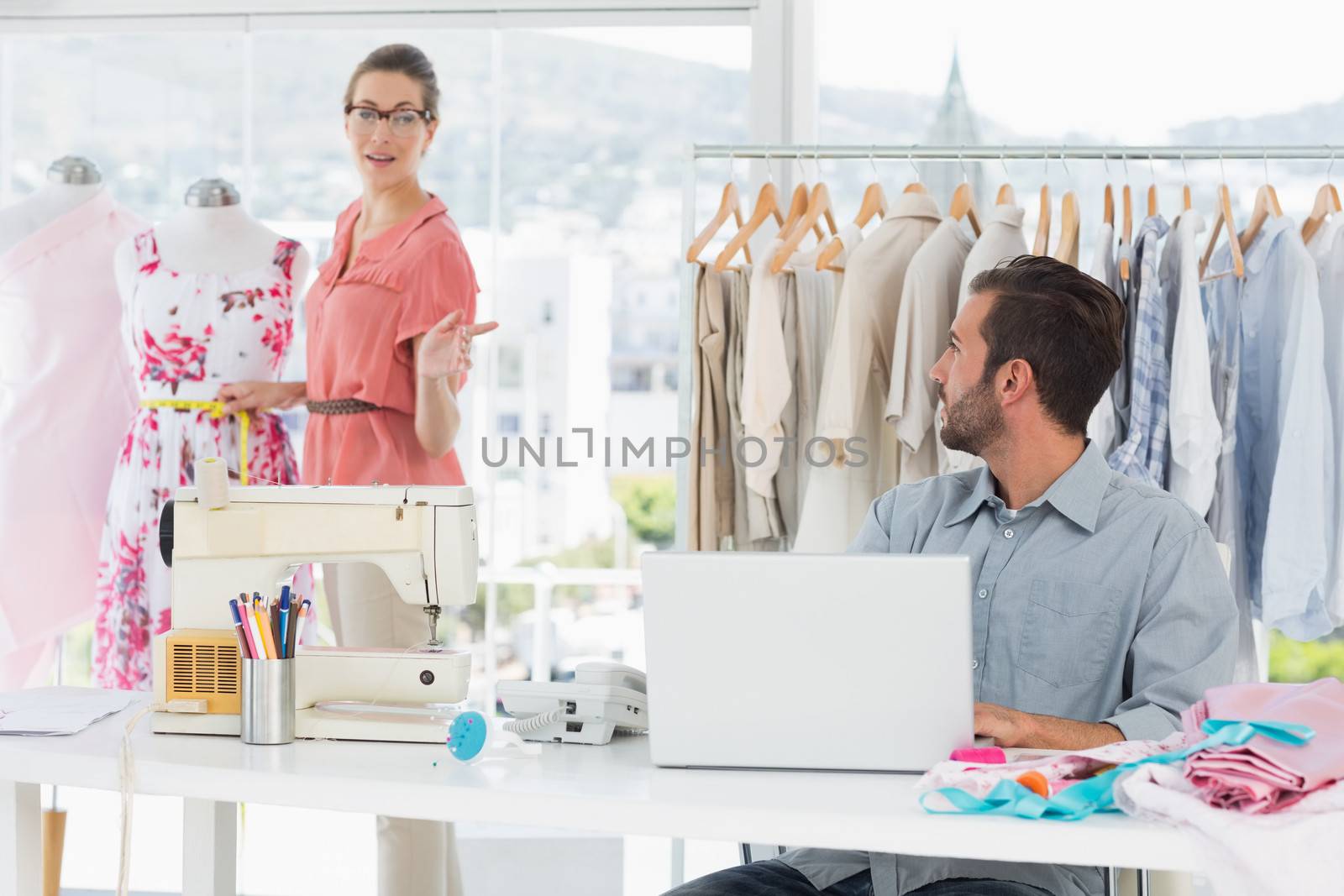 Young man using laptop with female fashion designer working in background at the studio