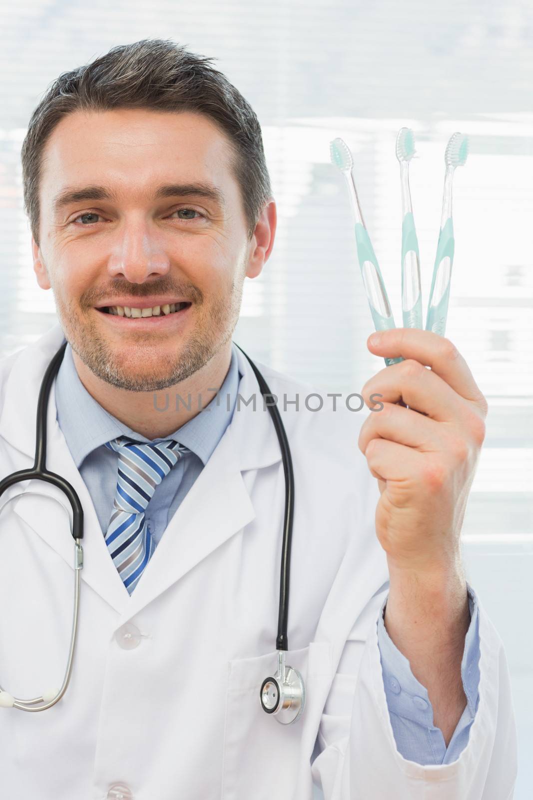 Smiling doctor holding toothbrushes in office by Wavebreakmedia