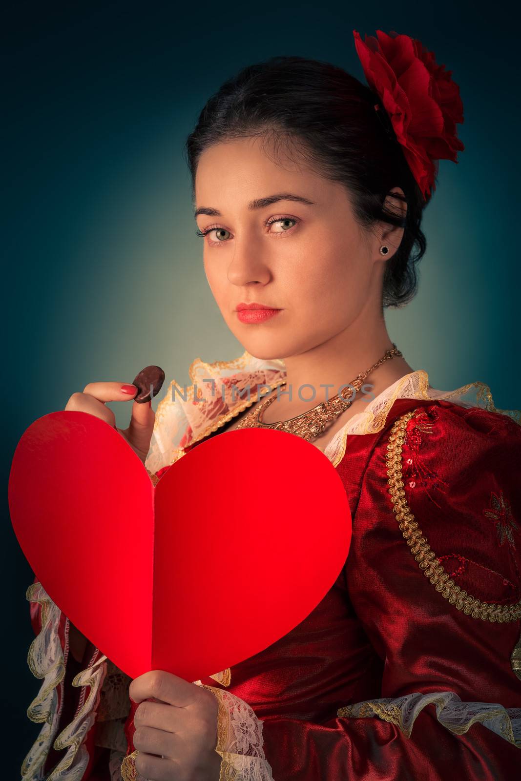 Portrait of a girl wearing a princess dress, holding a heart shaped card and a piece of candy.