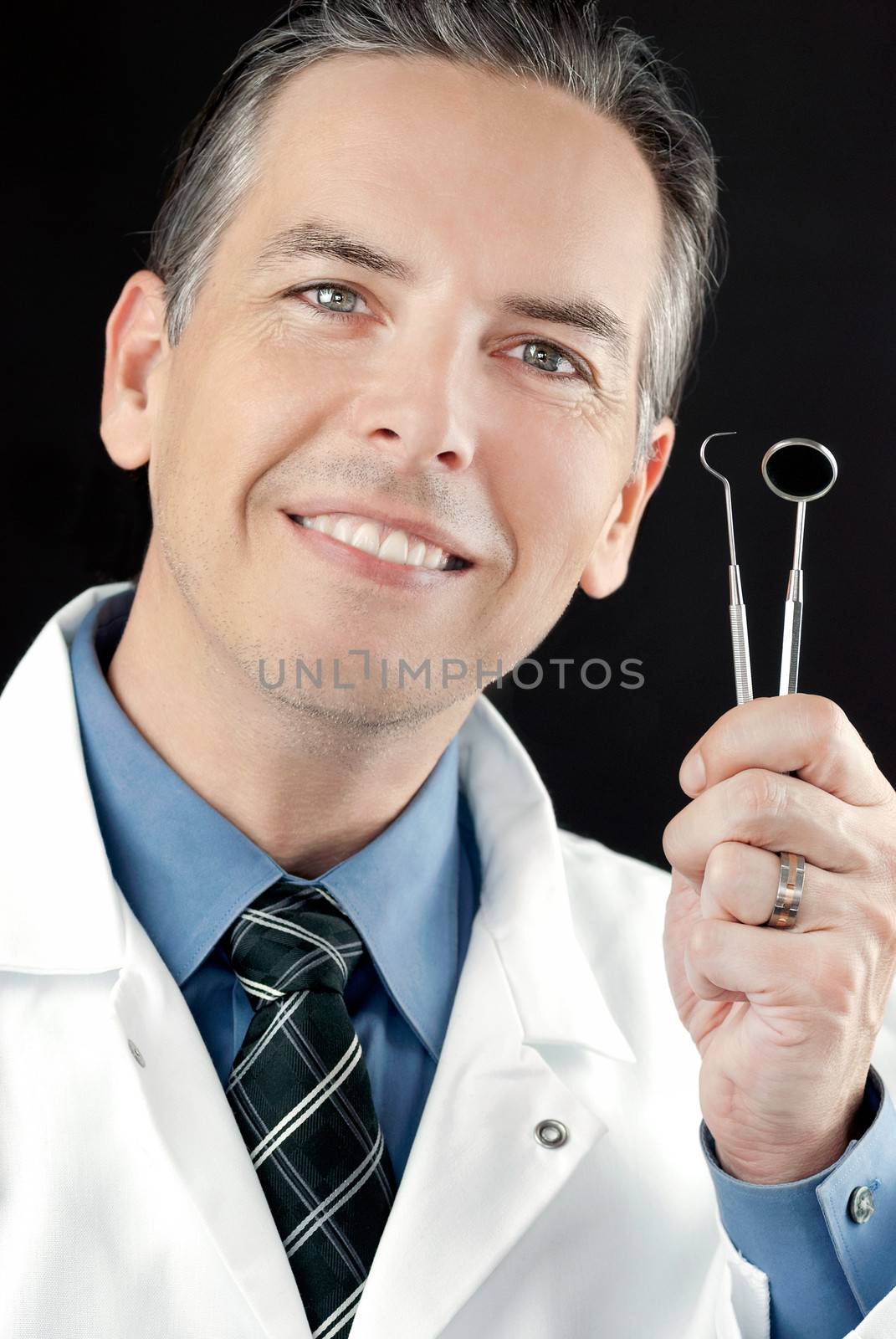 Close-up of a smiling dentist holding his tools