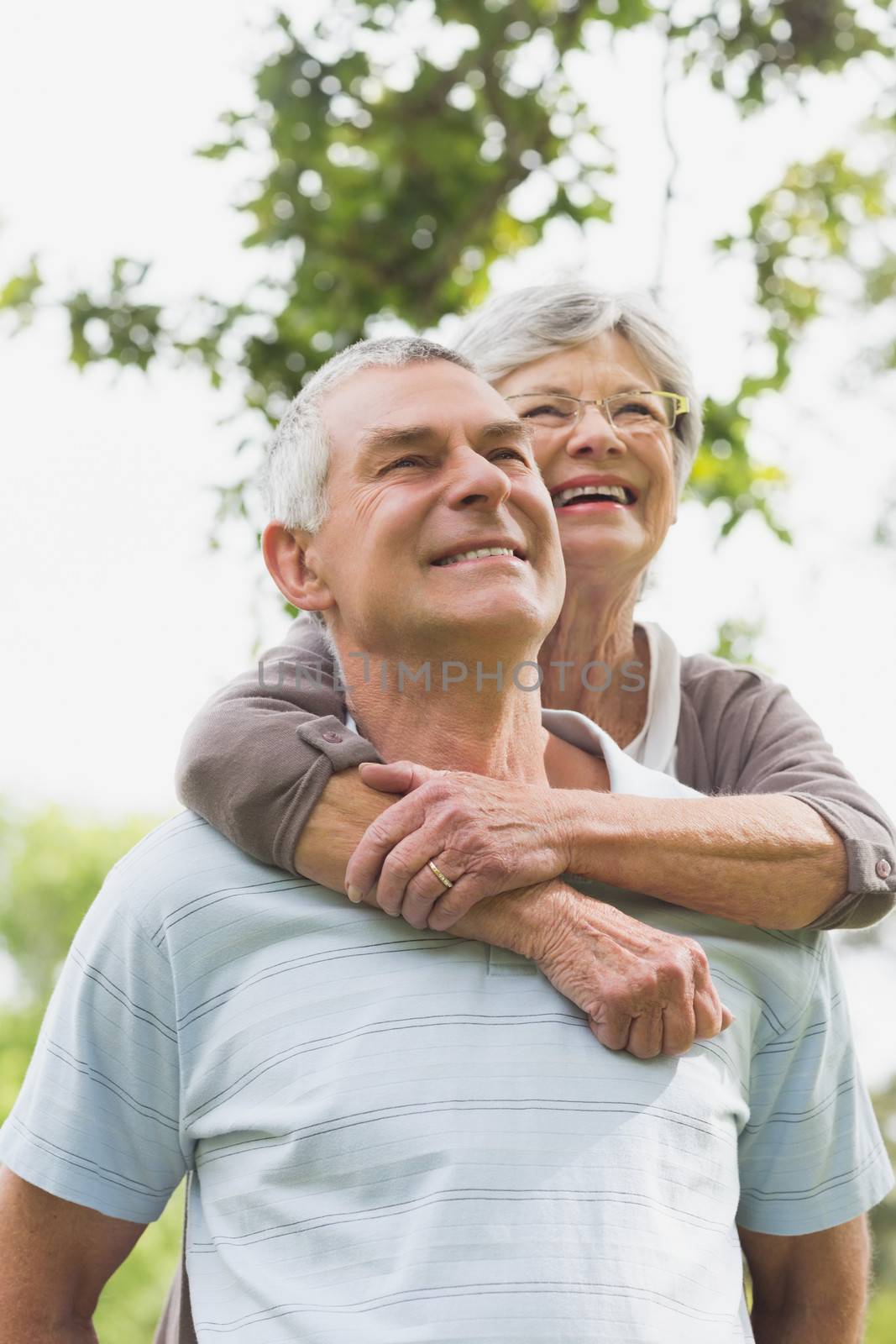 Happy senior woman embracing man from behind at the park