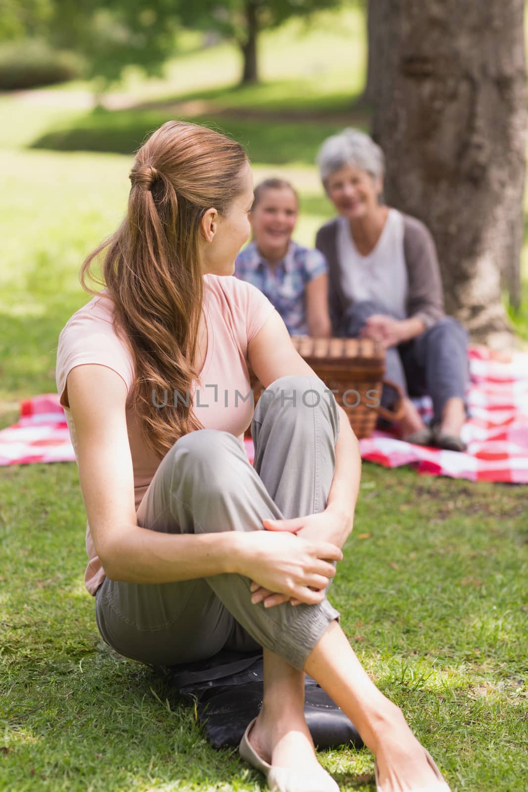 Portrait of a smiling woman with grandmother and granddaughter in background at the park