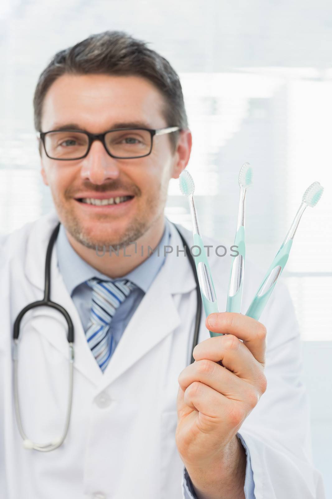Smiling doctor holding toothbrushes in office by Wavebreakmedia