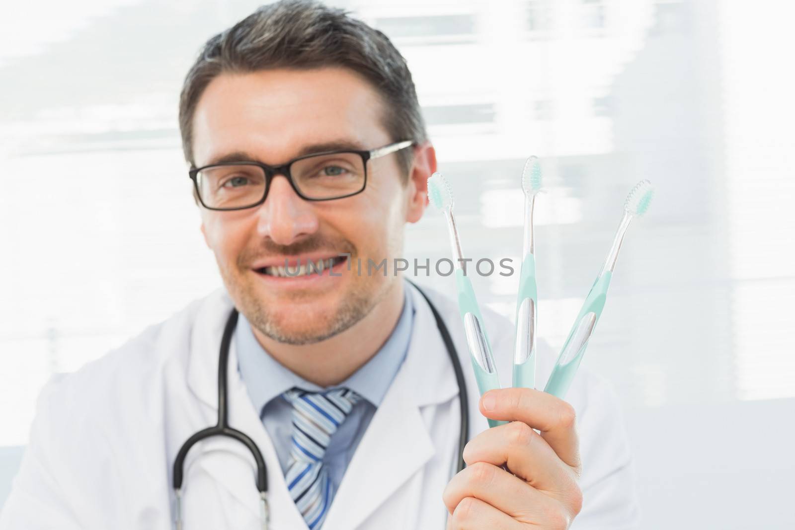 Closeup portrait of a smiling doctor holding toothbrushes in his office