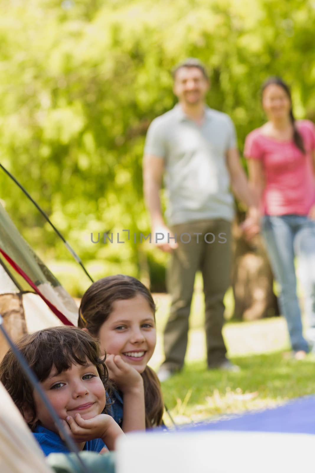 Portrait of kids in tent with blurred couple in background at park
