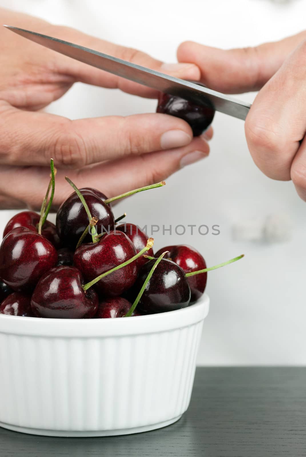 Close-up of a chef pitting a cherry in front of a bowl of cherries.