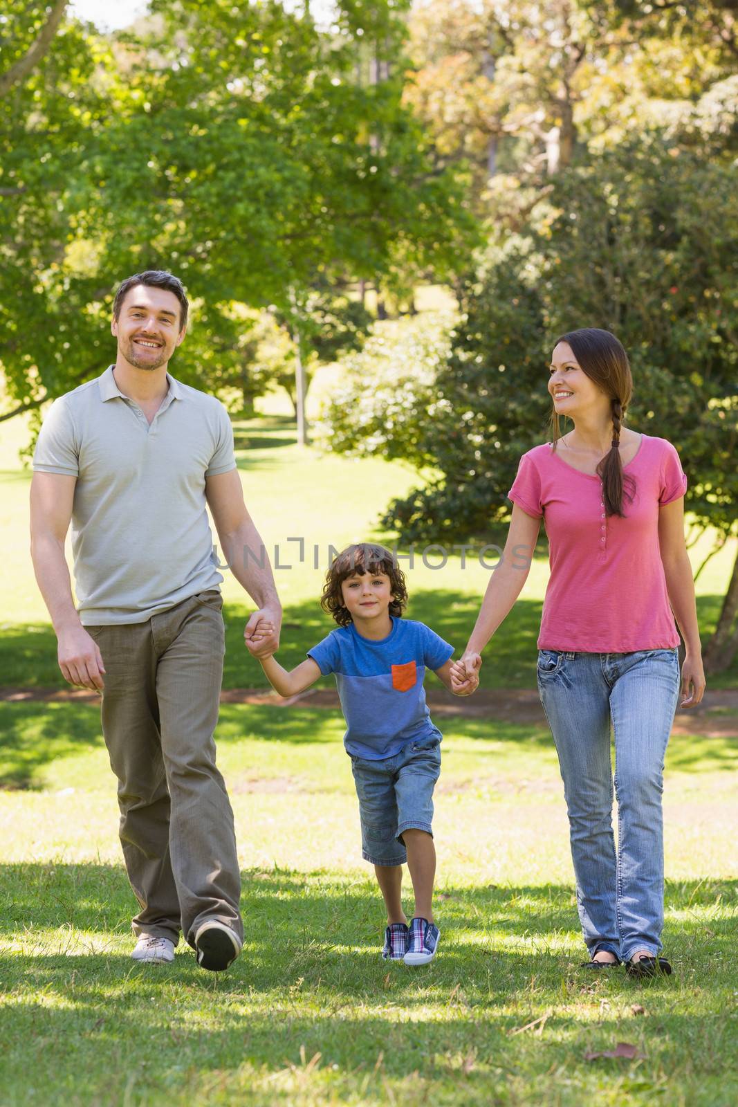 Family of three holding hands and walking at park by Wavebreakmedia