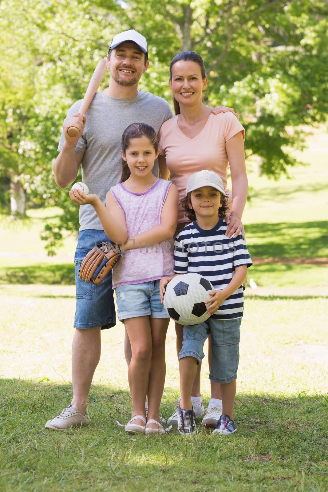 Family of four holding baseball bat and ball in park by Wavebreakmedia