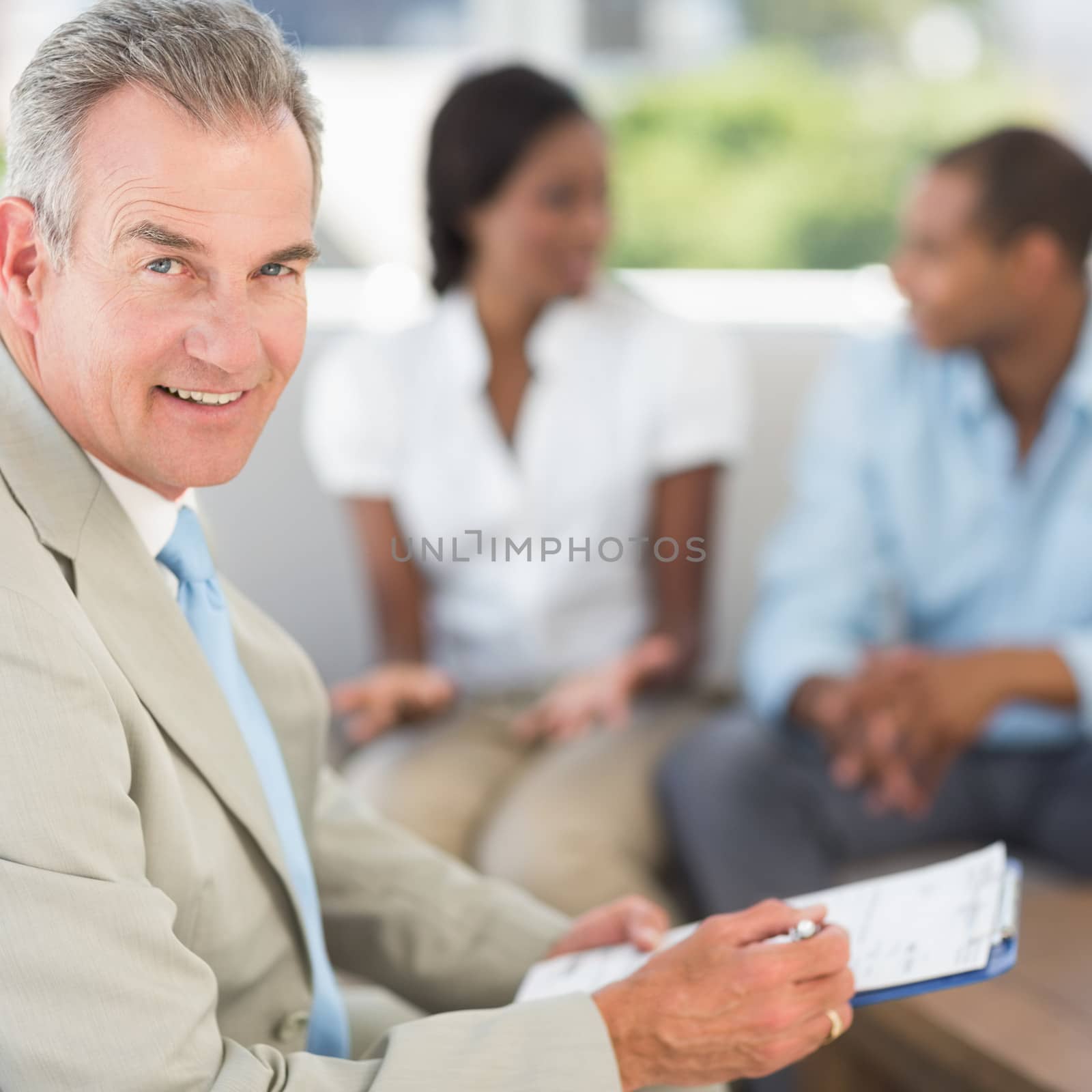 Salesman smiling at camera with couple behind him in the office