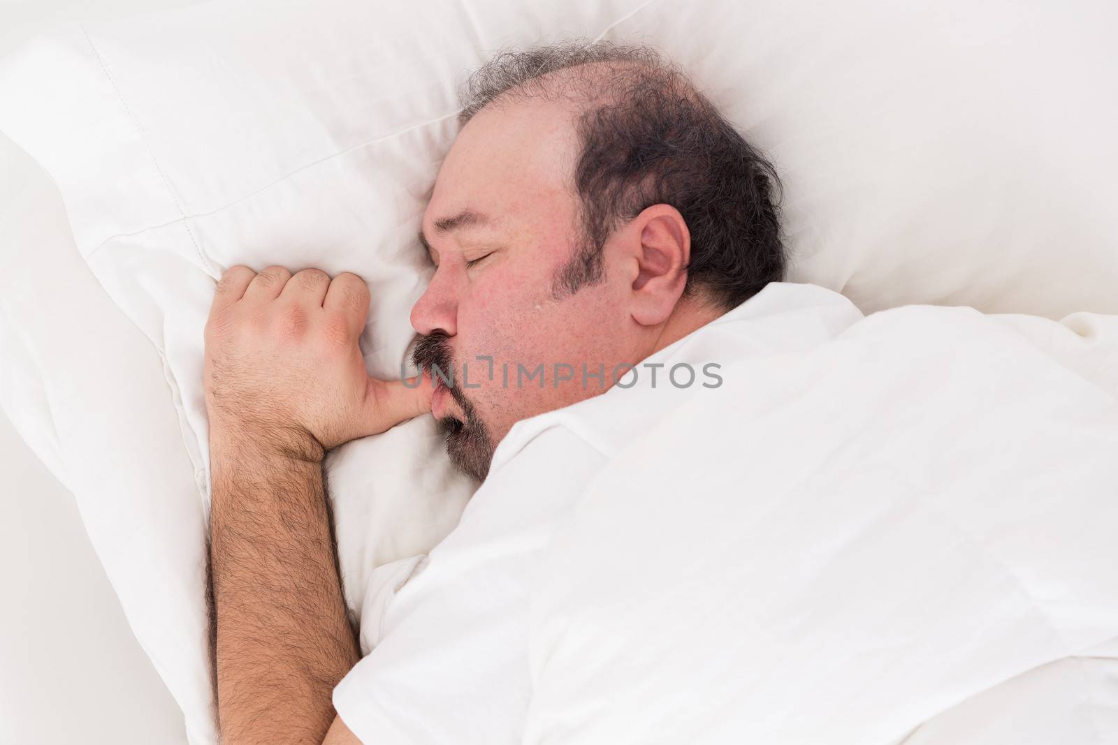 Closeup of a bearded man snuggling into his pillow sucking his thumb like a big baby while sleeping with a serene innocent expression