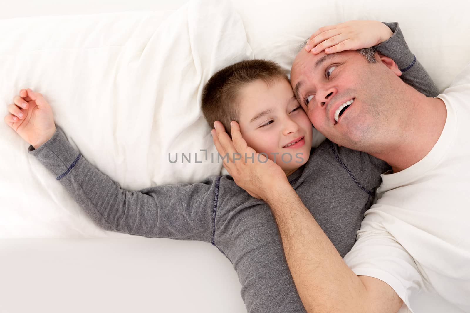 Father and his young son playing in bed cuddling with their heads close together smiling into each others eyes with affection