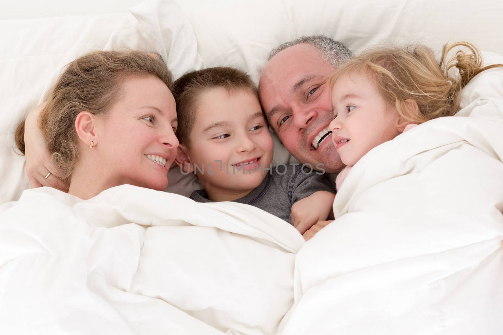 Happy young family cuddling together in bed by coskun