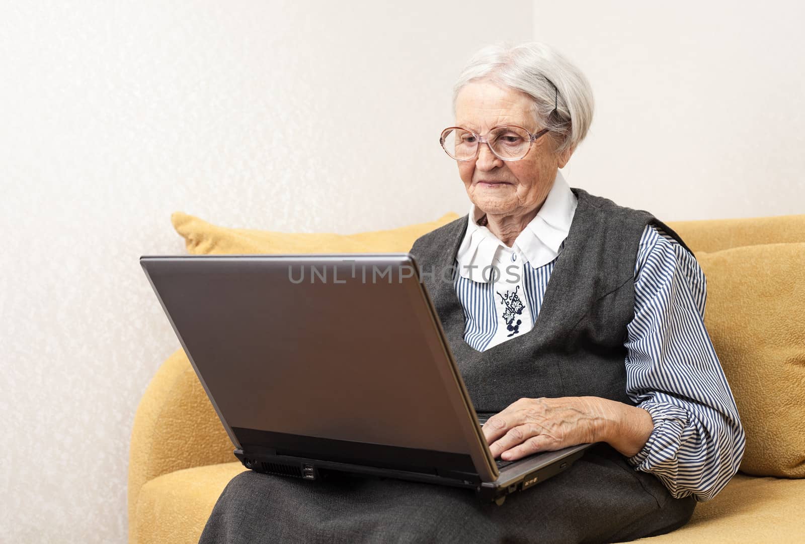 Senior woman using laptop computer sitting on sofa by photobac