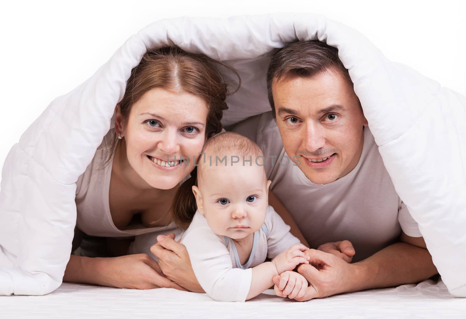 Young family with baby boy under blanket on bed by photobac