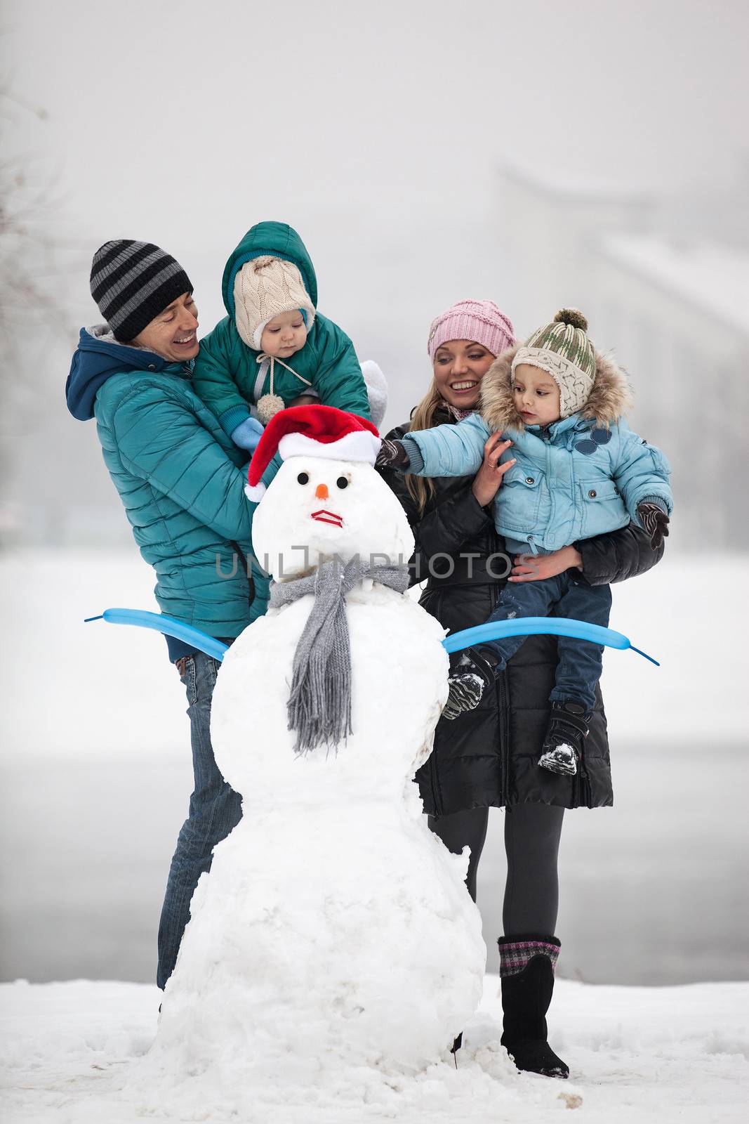 Caucasian family with two sons beside snowman outdoors