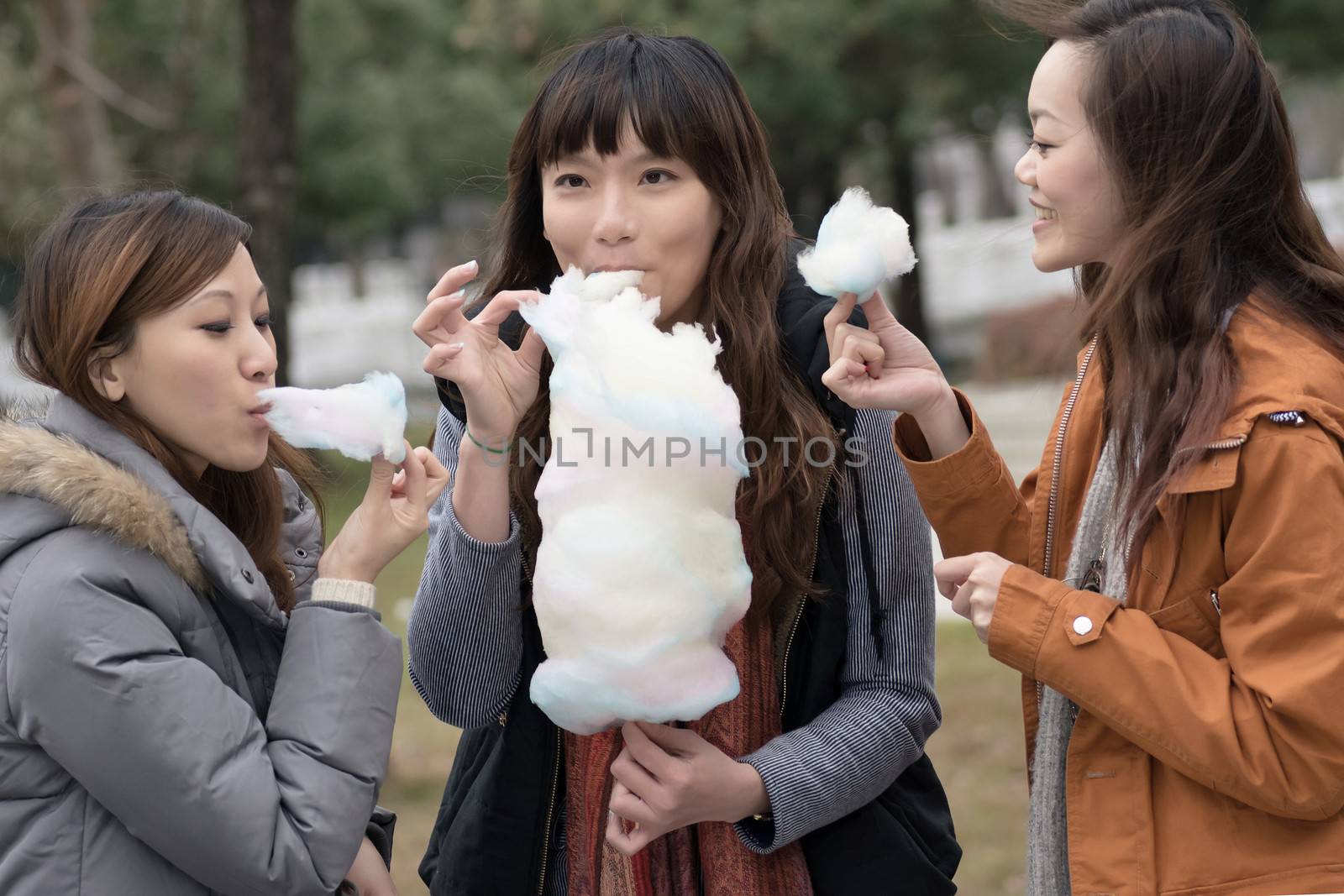 Happy young Asian woman eating cotton candy with her friends in outdoor.