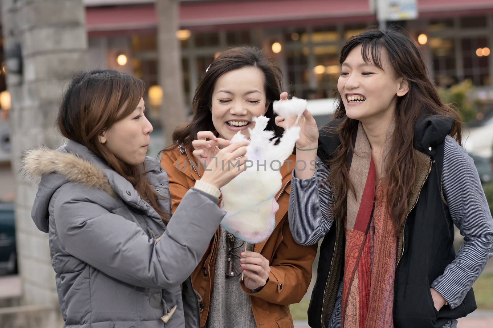 Happy young Asian woman eating cotton candy with her friends in outdoor.