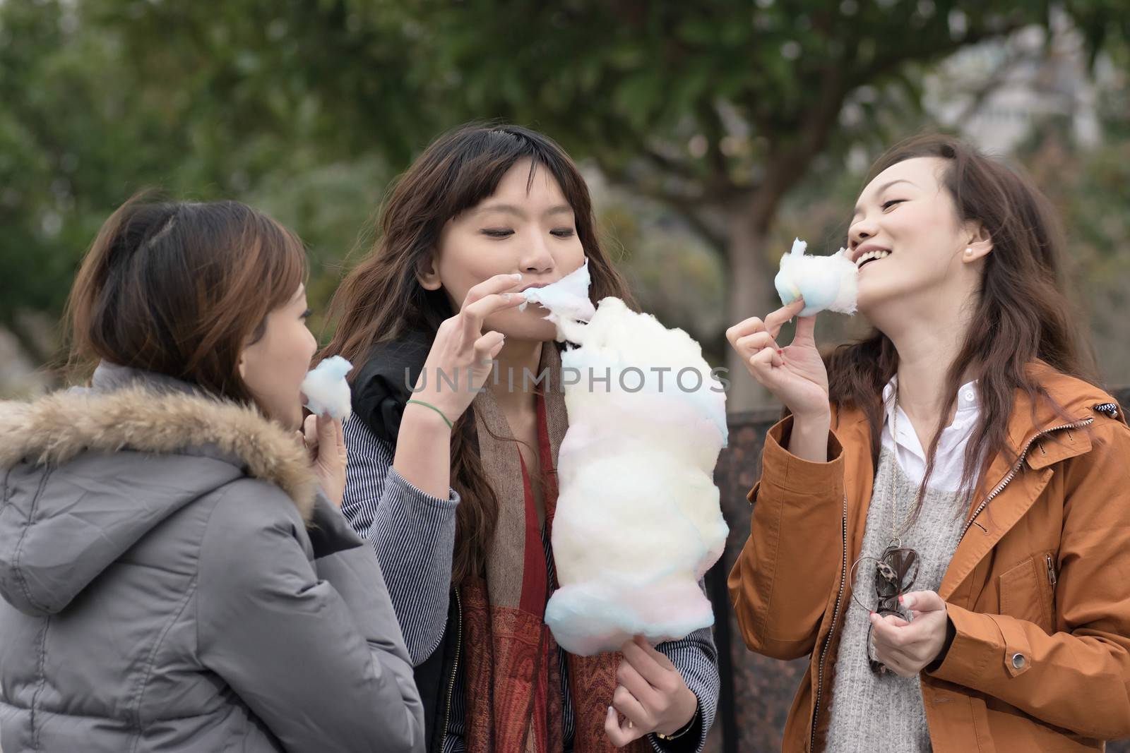 Happy young Asian woman eating cotton candy with her friends by elwynn