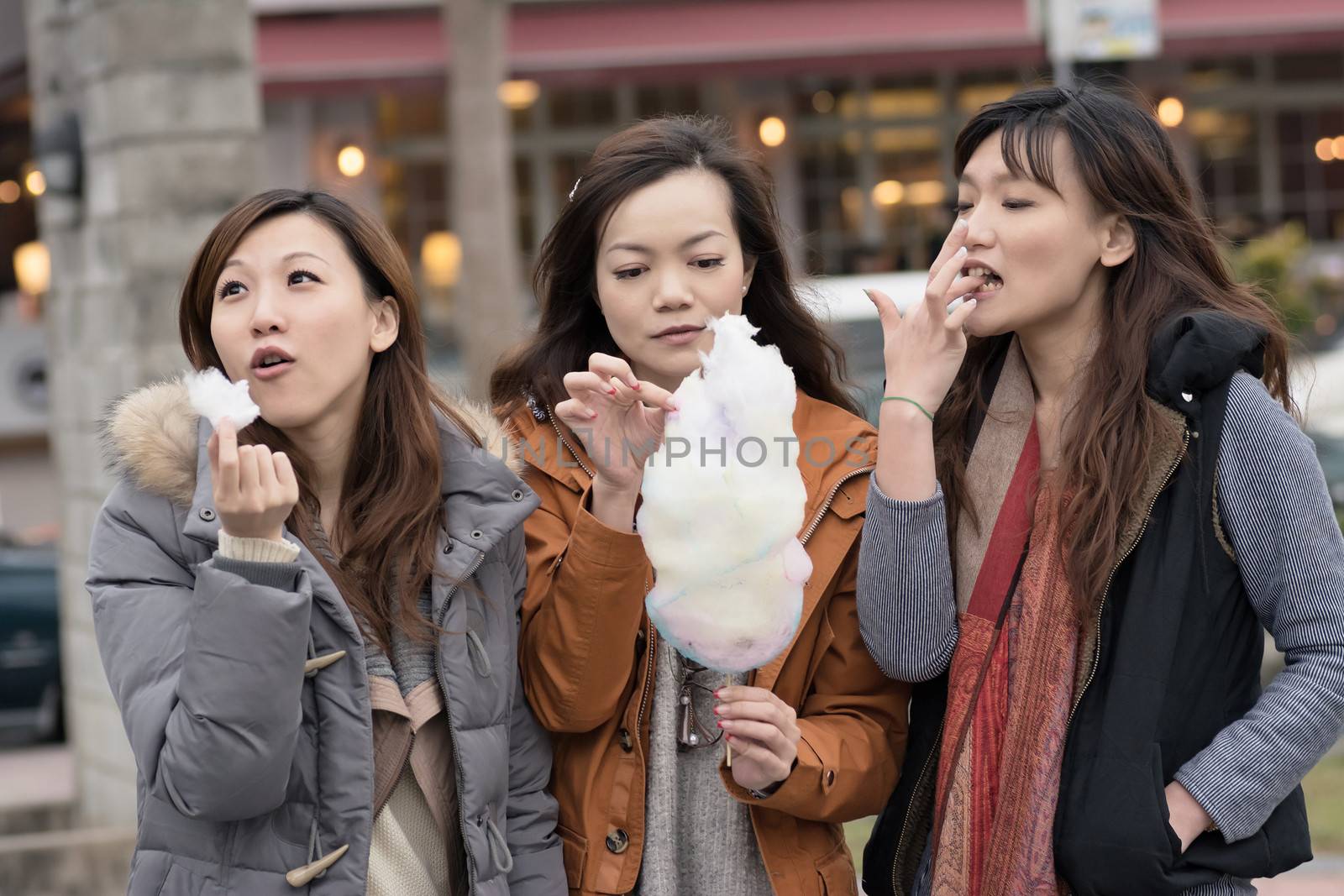 Happy young Asian woman eating cotton candy with her friends by elwynn
