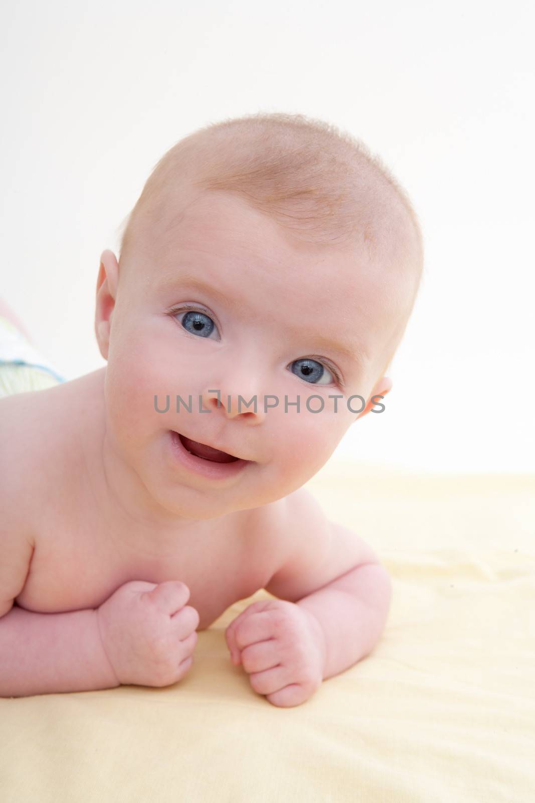 Bond little baby blue eyes lying down smiling on light yellow bed