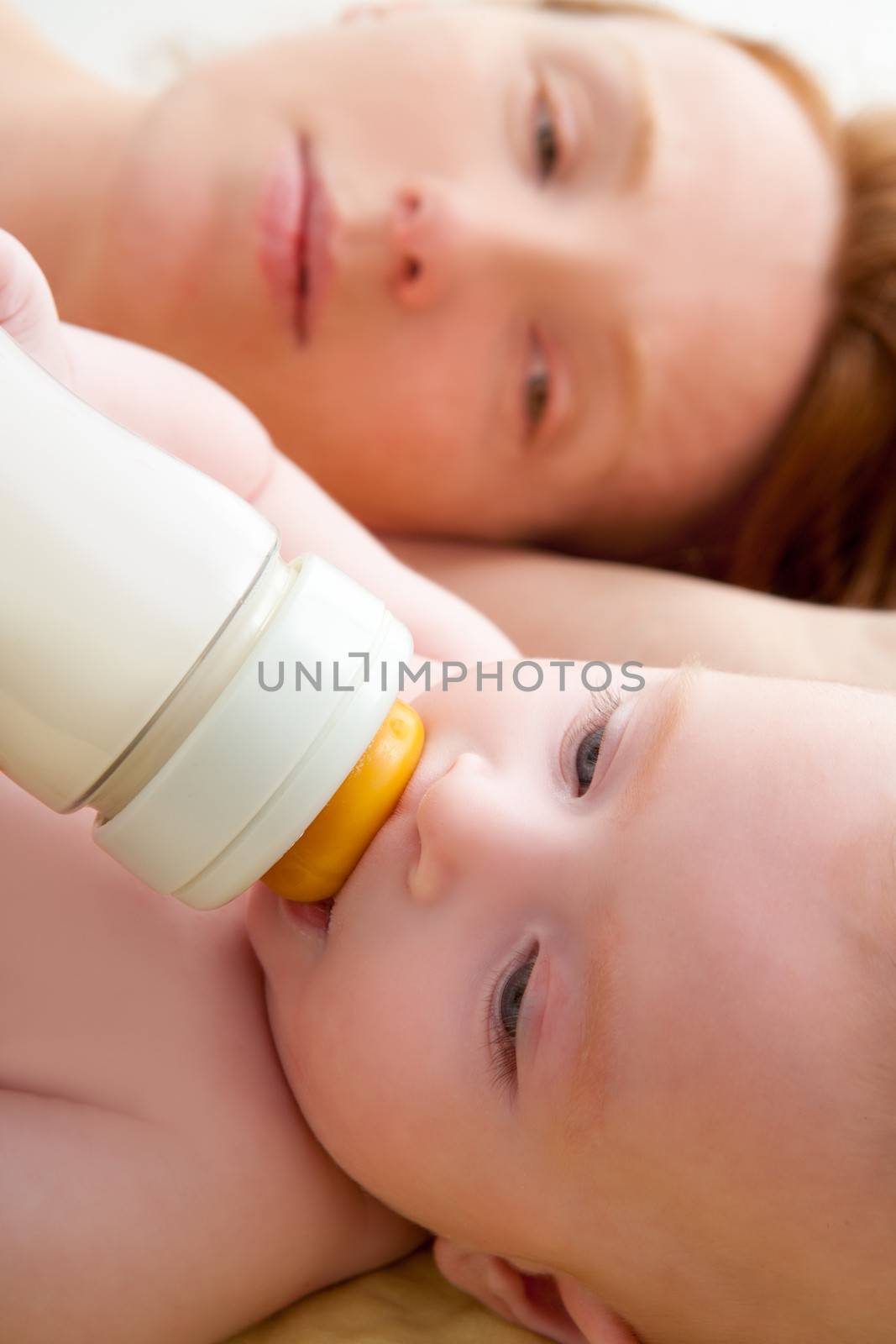 Bond little baby with blue eyes drinking bottle milk with her mother