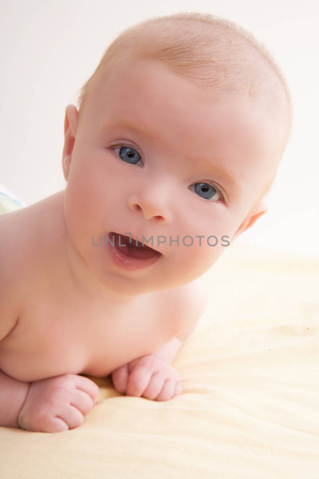 Bond little baby blue eyes lying down smiling on light yellow bed