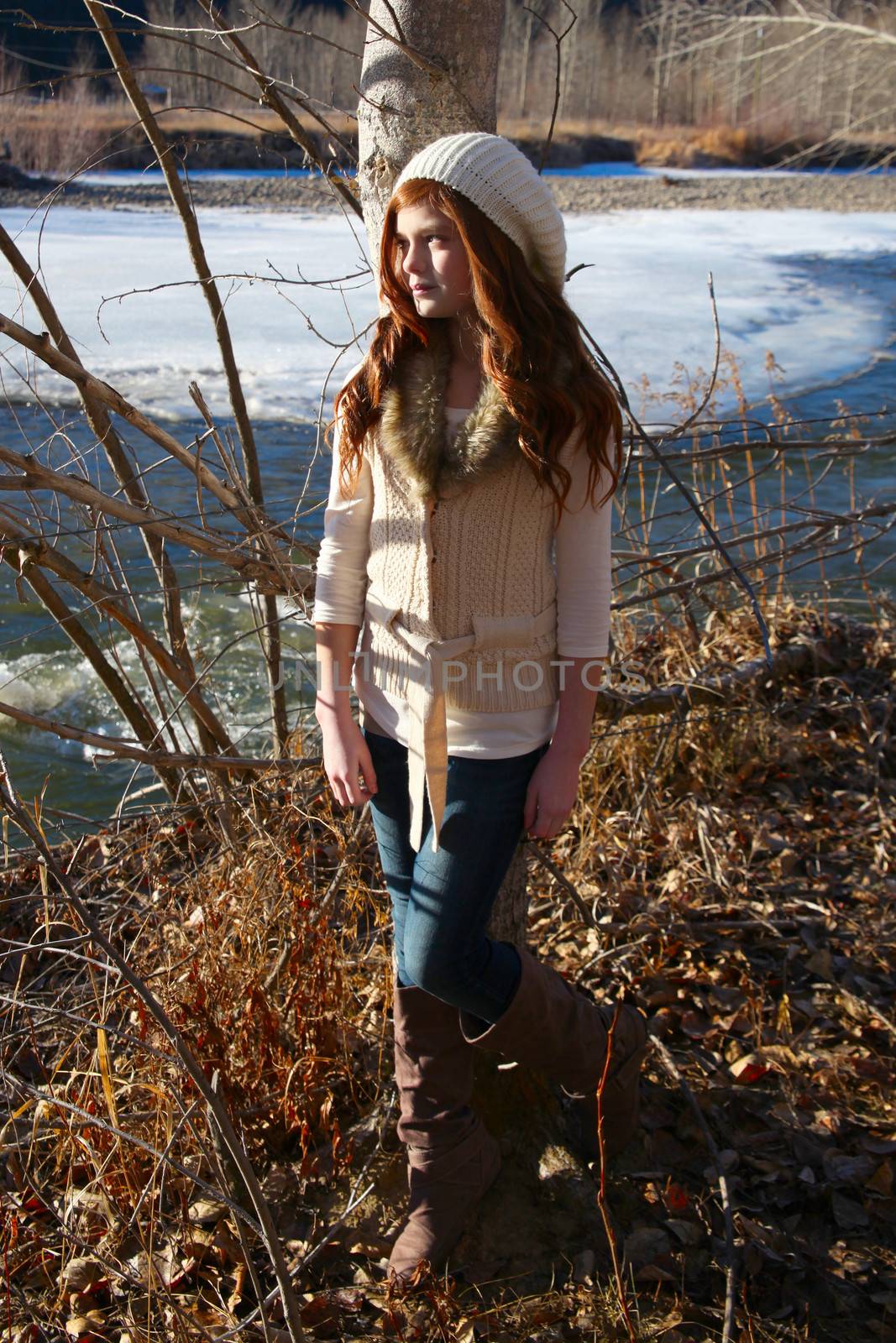 Winter girl leaning against a tree with river in the background