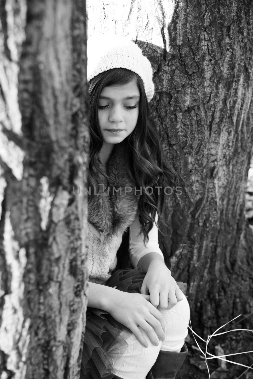 Winter girl sitting between two large tree trunks